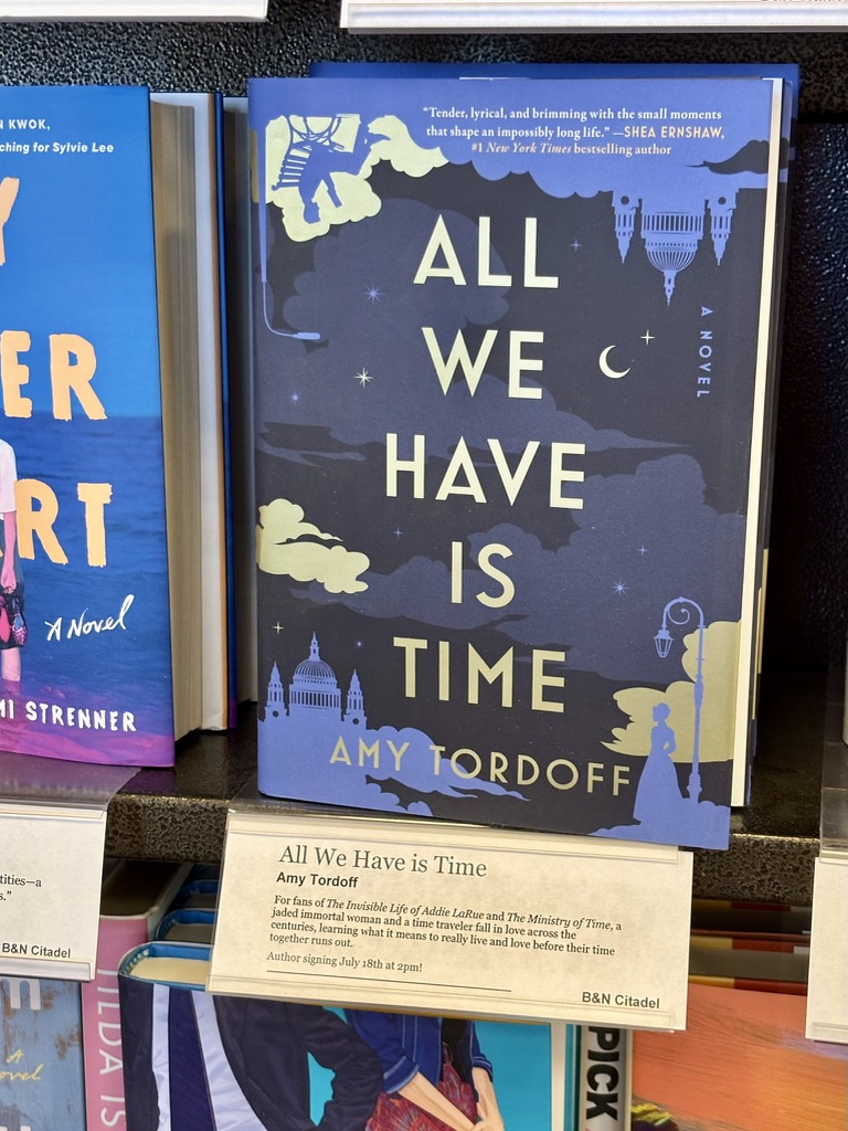 The book All We Have is Time on a shelf with a note from booksellers about the novel